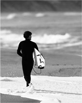 Surfer in wet suit and carrying a surfboard down the beach.